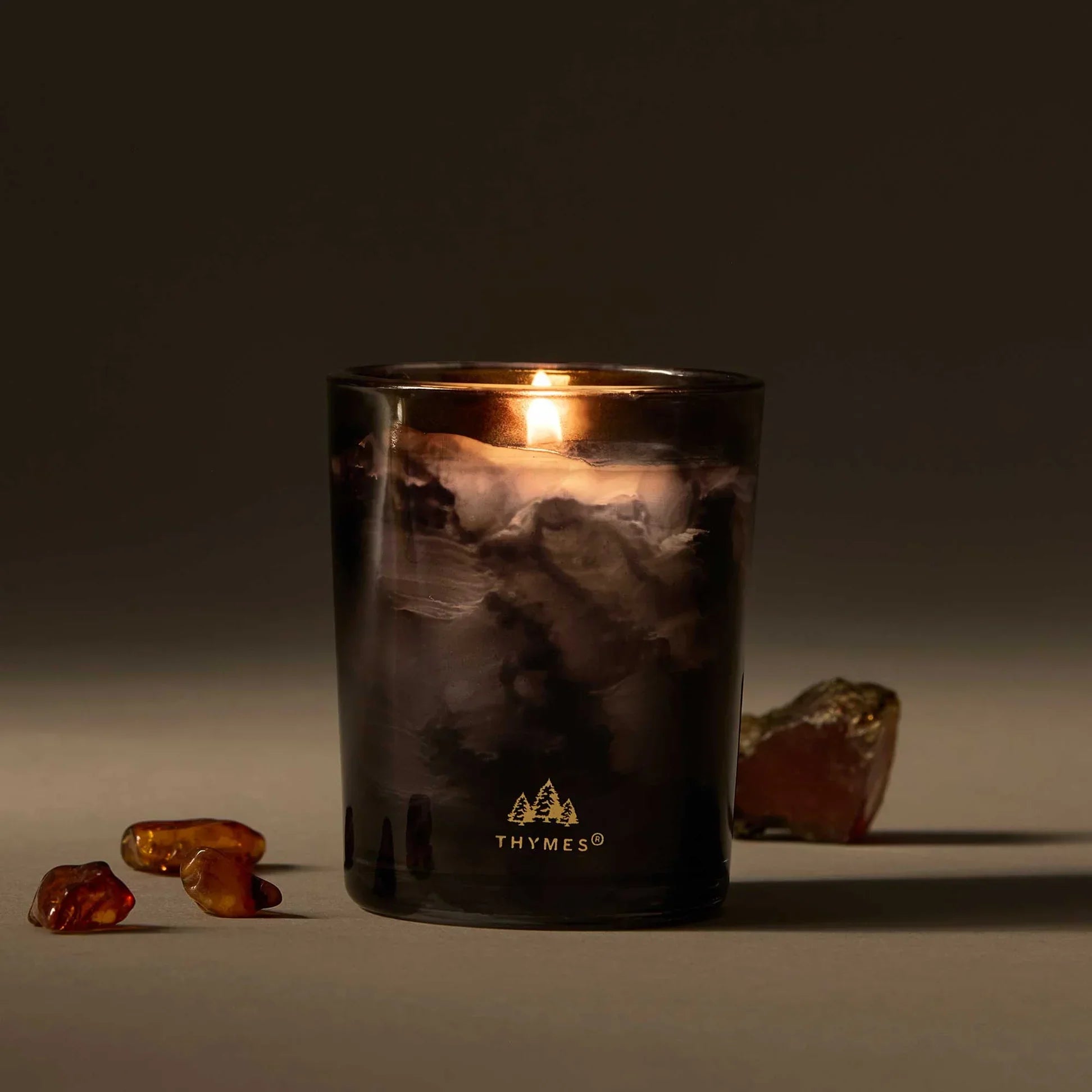 A Lit Noir Woods Votive Candle On Table 