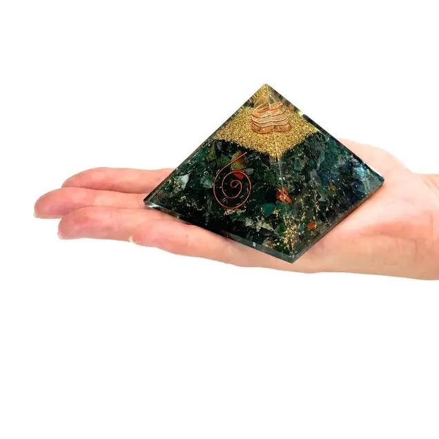 Hand holding a green crystal pyramid with intricate designs on a white background