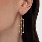 Gold earring with dangling Cubic Zirconias worn by a person