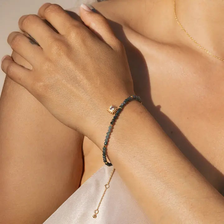 Close-up of a person's arm wearing a black beaded bracelet with a gold charm.