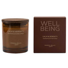 A candle in an amber glass jar with a dark wood lid sits next to its brown packaging box. The labels read 'CALM & SERENITY', 'Sandalwood & Petit Grain', and 'CERERIA MOLLA 1999'.
