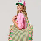 Woman holding a green and pink striped tote bag against a plain background