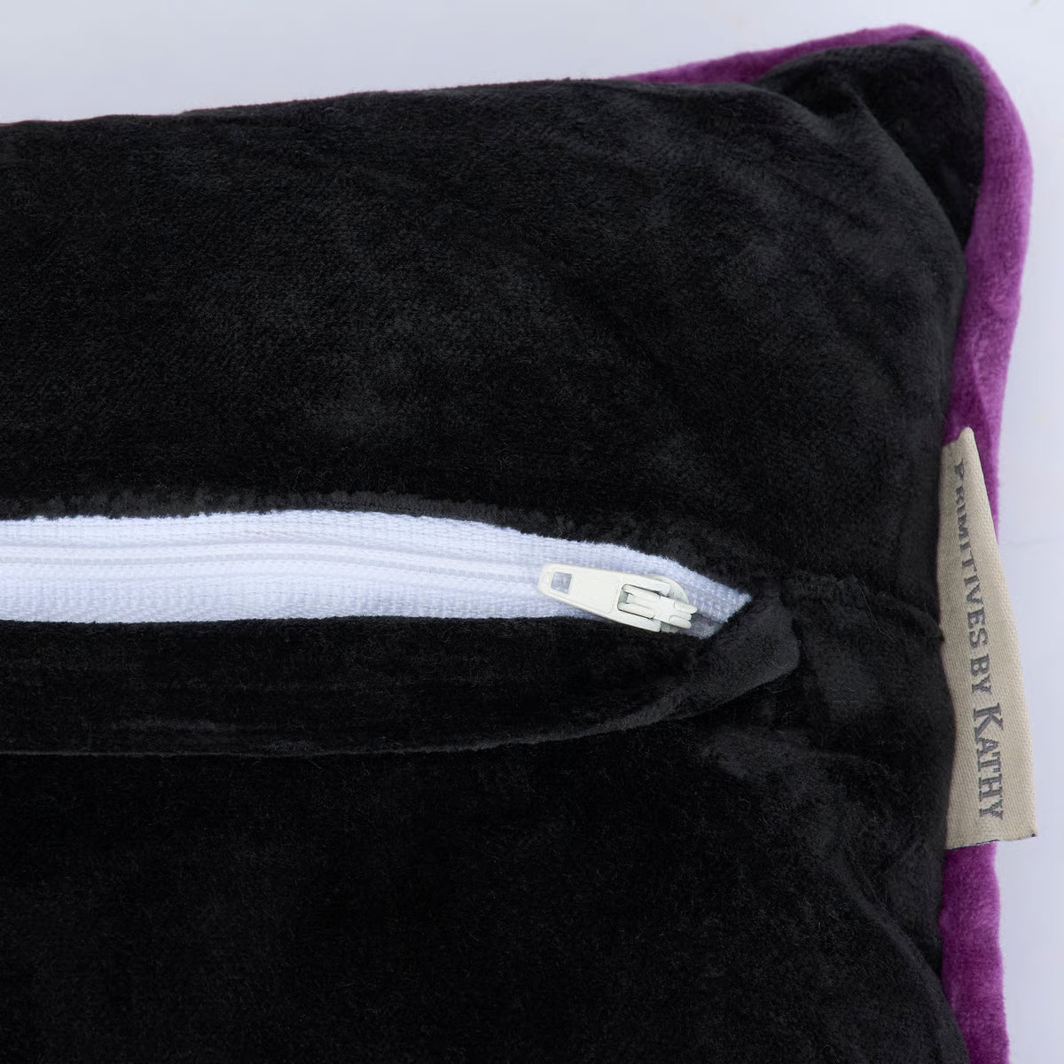 A close-up of a plush black cushion or pillow with a white zipper trim and a purple fabric edge visible on the right side.
