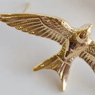 A close-up of a gold-toned bird pendant or brooch with spread wings, shown against a plain light background.