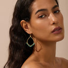 Woman wearing a gold earring with a green turquoise gemstone against a beige background