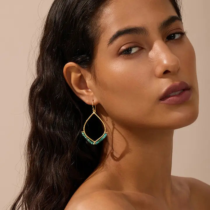Woman wearing a gold earring with a green turquoise gemstone against a beige background