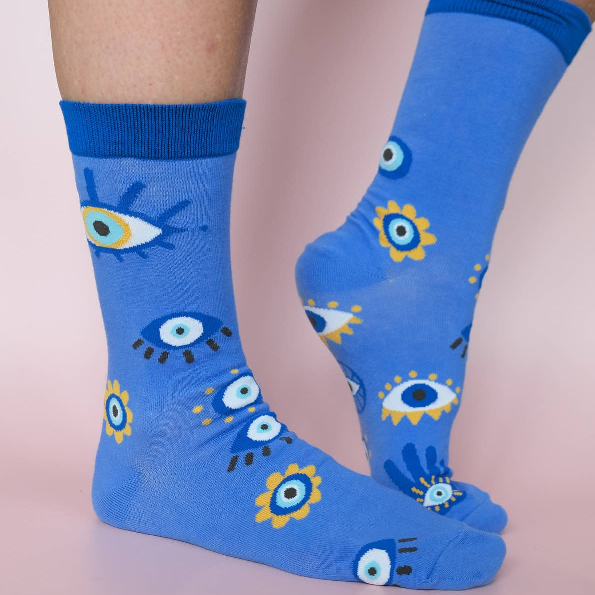 Blue socks with eye pattern worn by a person on a light pink background