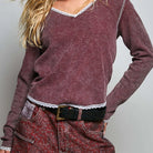 Woman wearing a patterned long-sleeve top and jeans against a plain background