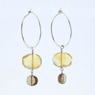 A pair of silver hoop dangle earrings featuring faceted yellow beads and smaller brown smoky beads, shown against a plain white background.