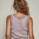 A woman shown from the back wearing a sleeveless textured top in a dusty mauve-pink color with lace trim along the neckline, paired with light-wash denim shorts.