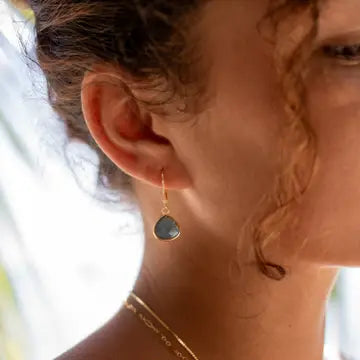 Close-up of a person wearing a gold earring with a dark labradorite stone pendant.