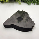 Black shungite stone with a circular depression on a white surface with greenery 