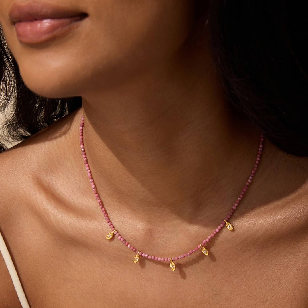 Close-up of a person wearing a pink Rhodonite beaded necklace with gold accents.