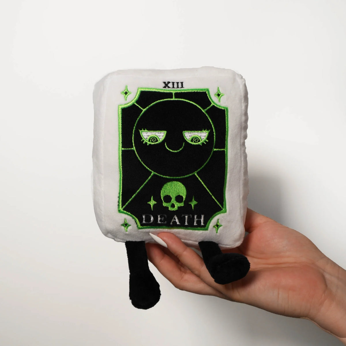 Plush toy with 'Death' card design held by a hand on a white background