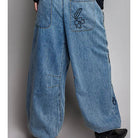 Wide-leg blue denim pants with a drawstring waist, back pockets, and embroidered rabbit motifs on the back pocket and side seam, shown on a model from the back against a gray studio background.