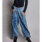 A woman modeling a black long-sleeve V-neck knit top and wide-leg blue denim pants with black floral embroidery, standing against a solid gray studio background.