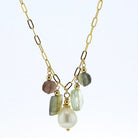 A gold chain necklace featuring a V-shaped arrangement of dangling gemstones, including a large white pearl, a light green stone, a pink stone, and a gray-green stone, set against a plain white background.