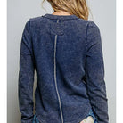 A woman shown from the back wearing a dark blue washed long-sleeve top with a central seam and a patch on the upper back, paired with distressed denim jeans.
