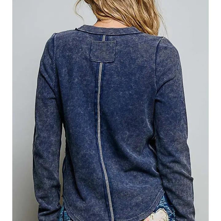 A woman shown from the back wearing a dark blue washed long-sleeve top with a central seam and a patch on the upper back, paired with distressed denim jeans.