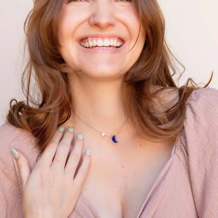 Woman wearing a necklace with a blue  lapis moon pendant against a plain background