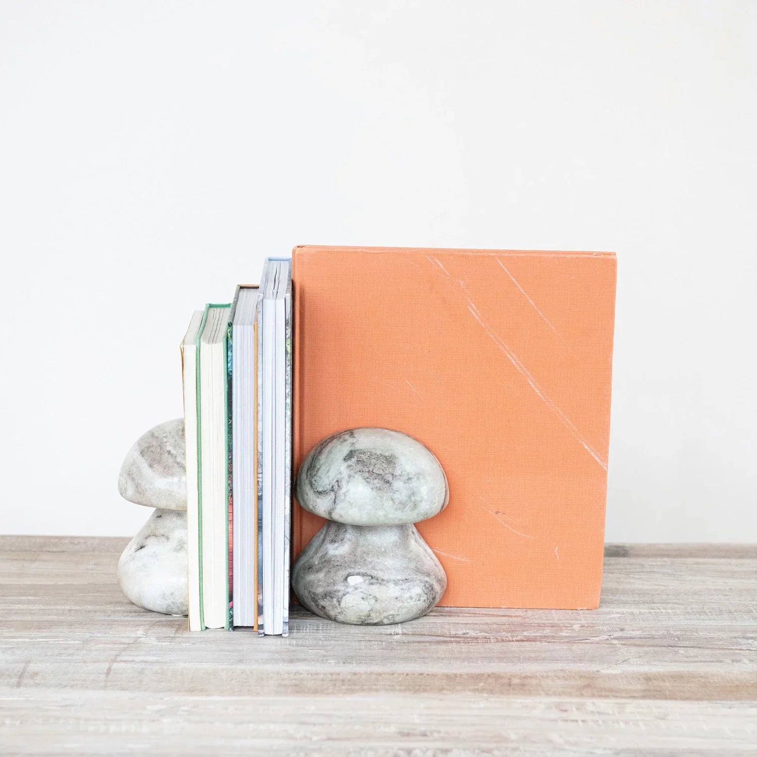 Stone mushroom bookends holding books on a wooden surface with a white background
