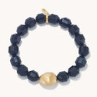 A beaded bracelet featuring faceted dark navy blue beads and one prominent matte gold accent bead, displayed on a clean off-white background.