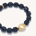 Faceted black beaded bracelet with a single large, smooth matte gold oval bead accent, photographed on a clean off-white background.