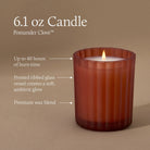 A lit 6.1 oz Pomander Clove candle in a frosted ribbed glass vessel, shown on a warm taupe background with callout text describing its burn time, glass finish, and wax blend.