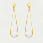 A pair of gold dangle earrings with a teardrop-shaped gold wire frame, a white faceted moonstone stone in the center, and a small round gold disc at the top, shown against a light off-white background.