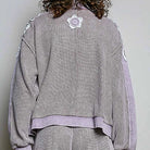 A person shown from the back wearing a matching gray and white houndstooth tracksuit with solid lavender-gray ribbed trim and a circular patch on the back collar, against a plain light gray background.