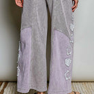 A person wearing a matching lounge set with a gray and white houndstooth pattern and light lavender panels and floral applique details, shown from the back against a neutral indoor background.