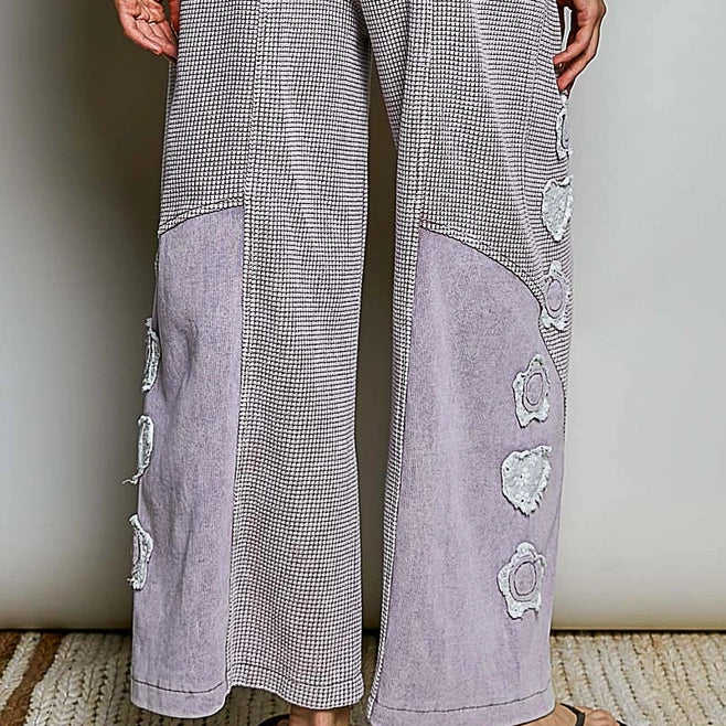 A person wearing a matching lounge set with a gray and white houndstooth pattern and light lavender panels and floral applique details, shown from the back against a neutral indoor background.