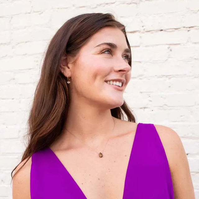 Woman wearing tiger eye necklace against a white brick wall